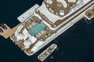 A luxurious yacht with a pool and lounge area is anchored in the deep blue sea, with a smaller tender boat nearby.