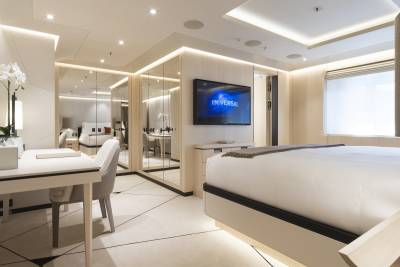 A luxurious bedroom with a desk and chair in the foreground and a large bed and mirrored wall in the background.