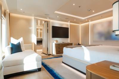 A luxurious bedroom with a chaise lounge in the foreground and a large bed and television in the background.
