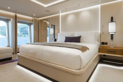 A luxurious bedroom with a large bed in the foreground and a scenic view of water and trees through the windows in the background.