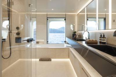 A modern bathroom with a sleek black countertop and sink in the foreground, and a bathtub with a large window overlooking a calm body of water and distant hills in the background.