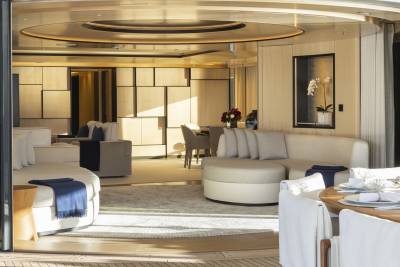 Luxurious cream-colored sofas and a dining table with white-covered chairs fill the foreground, while the background reveals a modern living space with geometric wall paneling and a circular ceiling design.