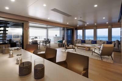 A modern yacht interior features a bar in the foreground and a spacious living area with a view of the ocean in the background.