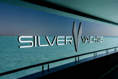 A sleek, metallic "SILVER YACHTS" logo floats above a tranquil turquoise ocean, framed by the dark, modern interior of a vessel.