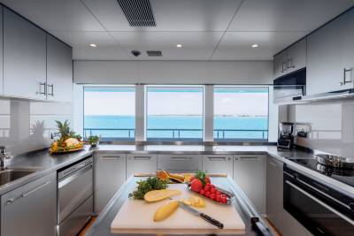A modern yacht kitchen with fresh produce on the island in the foreground and a panoramic view of the ocean through the windows in the background.