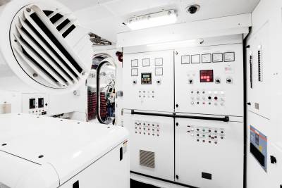 A large white generator dominates the foreground, while a complex control panel with numerous gauges and buttons fills the background.