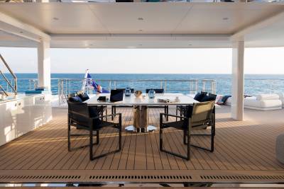 A modern outdoor dining set with chairs and a table sits on a wooden deck in the foreground, while the background reveals a vast expanse of the ocean under a clear sky.