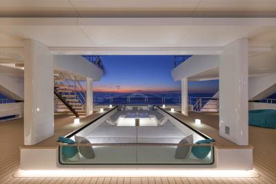A modern yacht's deck features a sunken seating area in the foreground, with a serene ocean sunset visible in the background.