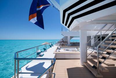 A luxurious yacht deck with turquoise water and a clear blue sky in the background, and a man standing near a hot tub in the foreground.