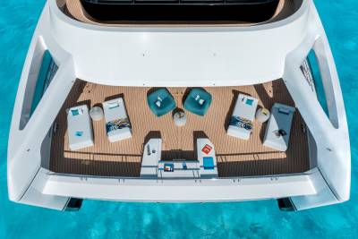 A luxurious white yacht with lounge chairs and sunbeds on its deck floats on crystal clear turquoise water.