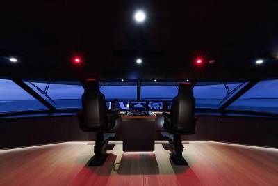 Two captain's chairs face a console of screens in a dimly lit yacht bridge, with the calm, blue ocean visible through the large windows.