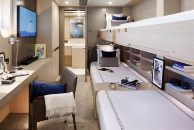 A modern cabin with two bunk beds in the foreground and a desk with a television in the background.