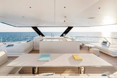 A white table with books sits on a yacht's deck in the foreground, with the ocean and sky visible in the background.