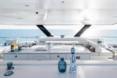A modern yacht's outdoor bar area with blue glass bottles in the foreground overlooks a calm ocean under a bright sky.