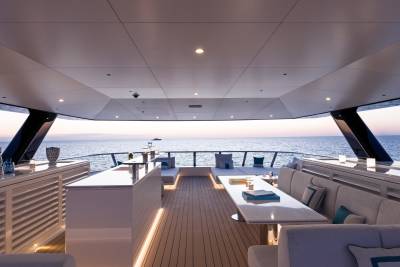 A luxurious yacht deck with a modern bar and seating area in the foreground overlooks a calm ocean at sunset in the background.