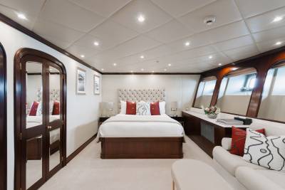 A luxurious yacht bedroom with a tufted headboard bed in the foreground and large windows overlooking the water in the background.