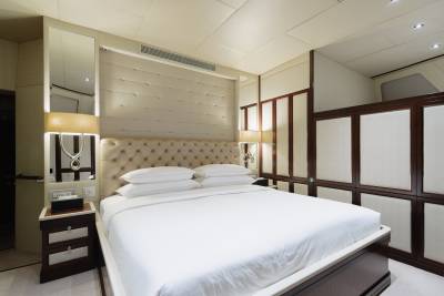 A neatly made bed with white linens dominates the foreground, while the background features a wall of built-in closets and a mirrored vanity.