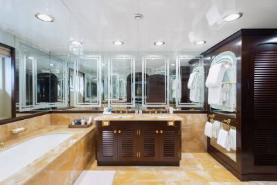 A luxurious bathroom features a marble bathtub in the foreground and a dark wood vanity with multiple mirrors in the background.