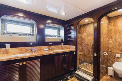 A luxurious bathroom with a double vanity in the foreground and a marble-tiled shower and toilet in the background.