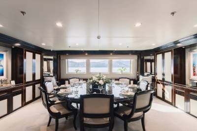 A formal dining table set for a meal is in the foreground, while a scenic view of islands and water is visible through the windows in the background.