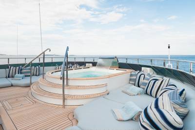 A luxurious yacht's sundeck features a bubbling jacuzzi with a waterfall in the foreground, while the background shows a calm blue ocean under a cloudy sky.