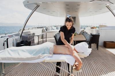 A woman receives a massage on a yacht deck with the ocean and sky in the background.