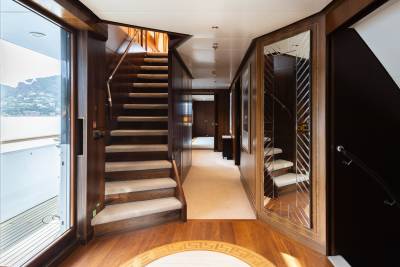 A luxurious yacht hallway features a carpeted staircase in the foreground and a long, well-lit corridor with mirrored walls in the background.