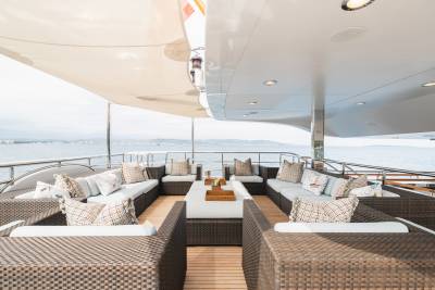 Wicker furniture with plush cushions is arranged on a yacht's deck, overlooking a calm ocean under a white canopy.