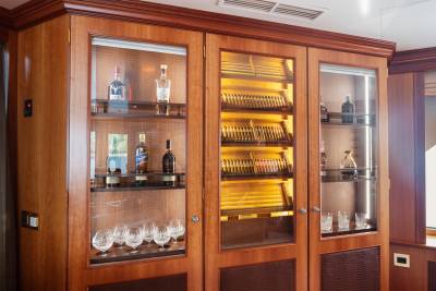 A wooden cabinet with glass doors displays bottles of liquor and cigars in the foreground, while the background shows a continuation of the wooden interior.