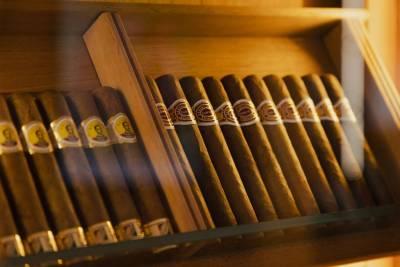 A close-up view of a wooden humidor filled with rows of cigars, with the foreground showing the banded ends of the cigars and the background revealing the interior of the humidor.