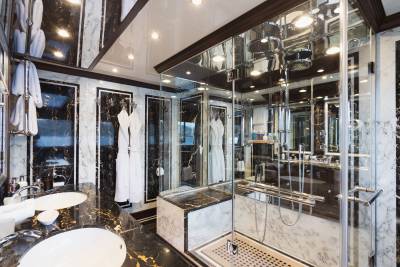 A luxurious bathroom with marble countertops and sinks in the foreground, and a glass-enclosed shower with reflections of the opulent interior in the background.