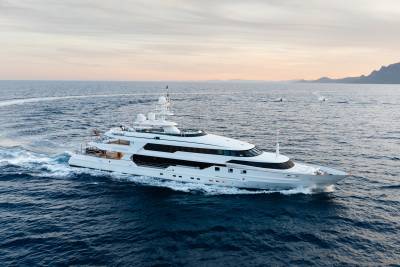 A large white yacht cruises through the deep blue ocean, with a hazy coastline visible in the distance under a soft sky.