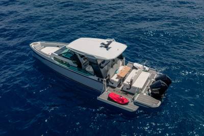 A white motorboat with a red life raft on its extended swim platform floats on the deep blue ocean.