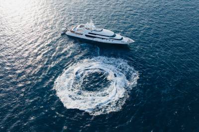 A large white yacht cruises on a deep blue ocean, leaving a circular wake in its path.