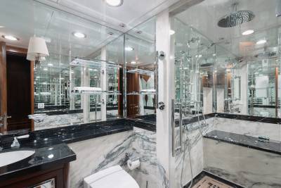 A luxurious bathroom with a marble vanity and toilet in the foreground is reflected in mirrored walls that extend to a glass-enclosed shower in the background.