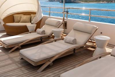 Sun loungers and a cabana on a yacht's deck overlook a sparkling blue ocean and distant islands.