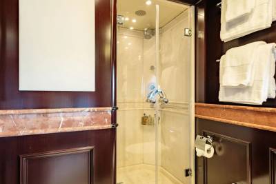 A luxurious bathroom features a glass-enclosed shower in the center, with dark wood paneling and marble accents surrounding it.