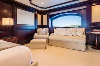 A luxurious bedroom with a plush bed in the foreground and a large window in the background revealing a scenic view of rolling green hills under a bright blue sky.