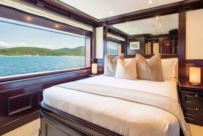 A luxurious bedroom with a large window overlooking a serene seascape and lush green hills.