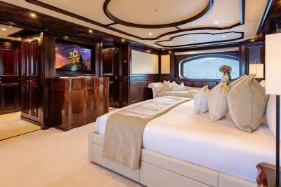 A luxurious bedroom with a large bed in the foreground and a large window with a view of the sea in the background.