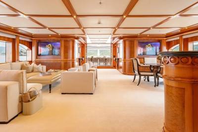 Plush white sofas and a dining set occupy the foreground of a luxurious yacht's lounge, while large windows reveal a serene, water-filled background.
