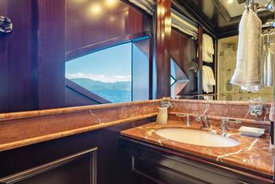 A luxurious bathroom with a marble vanity and sink in the foreground is reflected in a mirror, revealing a stunning ocean view with distant mountains in the background.
