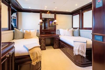 Two beds with plush pillows and blankets are in the foreground, while a vanity with mirrors and ornate wooden paneling fills the background of this luxurious cabin.
