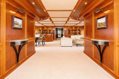A plush carpeted hallway with ornate wooden paneling and wall sconces leads to a well-lit lounge area with comfortable seating and display cabinets.