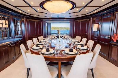 A formal dining table set for a feast is centered in a richly paneled room, with a large window in the background revealing a serene ocean view.