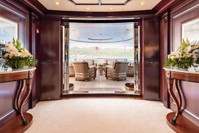 Luxurious mahogany-paneled hallways with floral arrangements on ornate tables lead to an open deck area with comfortable seating and a scenic view.