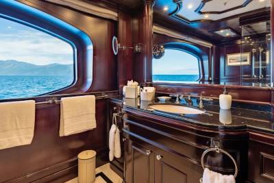 A luxurious yacht bathroom with dark wood paneling and a marble countertop in the foreground, and a stunning ocean view through large windows in the background.