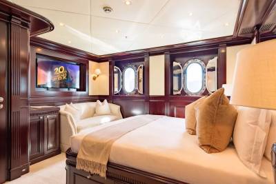 A luxurious yacht bedroom features a plush bed in the foreground and ornate wooden paneling with oval windows in the background.