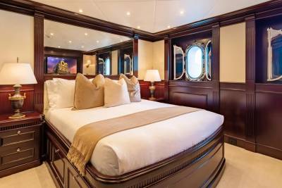 A luxurious bedroom with a large bed in the foreground and ornate wooden paneling and windows in the background.
