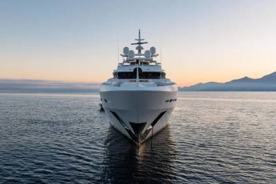 A large white yacht is anchored in calm water with a hazy mountain range in the background under a soft sky.